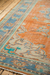 Distressed Oushak rug showing tangerine orange field, sky blue border, and visible foundation.