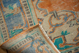 Folded distressed Oushak rug edge showing worn pile, tangerine, sky blue, and mint green.