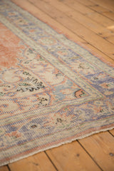Distressed Oushak rug with faded dusty peach field and pale royal blue scalloped border.