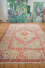 Vintage Oushak carpet viewed at an angle, showing its distressed seafoam green field and blush medallion.