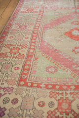 Angled view of a distressed Oushak carpet's geometric border in raspberry red and seafoam green.