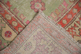 Corner of a distressed Turkish Oushak rug reveals its hand-knotted foundation and low pile.