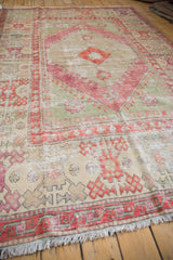 The corner of a distressed Oushak rug, showing its geometric border and time-softened texture.
