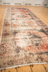 Distressed Oushak runner's worn texture, faded brick red, navy charcoal, and ivory paneled guls.