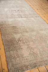 Distressed Oushak runner corner, revealing faint multi-panel geometric pattern in rose, beige, and silver with fringe.