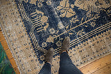 Distressed Oushak rug with navy blue and beige reciprocating motifs showing heavy wear.