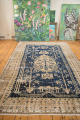 Distressed Oushak carpet displaying a beige tree of life medallion on a dark blue field.