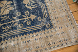 Distressed vintage Oushak rug corner, with exposed foundation, navy blue motifs, and beige fringe.