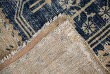 Corner of hand-knotted vintage Oushak rug, showing distressed navy pile, fringe, and woven foundation.