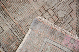 Folded vintage distressed Oushak rug runner, showing worn pile, fringe, and woven foundation.
