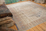 Distressed Oushak carpet corner with denim blue border, worn ivory field, and fringe.