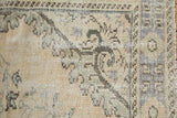 Corner of distressed Oushak rug with faded blue Rococo motifs and low, even pile.