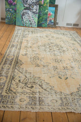 Distressed Oushak rug corner with pale beige tones, faded Rococo florals, and visible knot head wear.