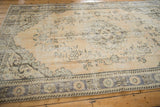 Corner of distressed vintage Oushak carpet showing faded blue border and worn beige field.