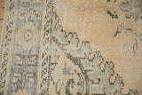 Distressed Oushak rug's worn fringe and faded border with pale sand and muted green patterns.