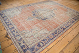 Distressed Oushak rug corner, showing faded rust field, navy border, and worn texture.