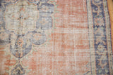 Close-up of vintage Oushak rug's distressed texture, showing wear with pale terra cotta, navy, and ivory patterns.
