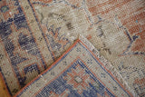 Distressed Oushak rug corner with worn pile, visible foundation, navy, terra cotta, ivory.