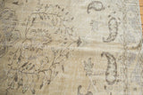 Distressed vintage Oushak carpet corner featuring worn ivory, beige, brown vinery, boteh motifs, and fringe.