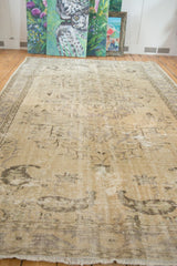 Distressed vintage Oushak carpet, faded vinery and boteh patterns in muted beige and mauve.