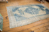 Distressed Oushak rug corner featuring faded blue patterns, ivory tones, and woven fringe.