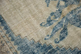 Distressed Oushak carpet with worn pile, blue serrated floral design on a beige field.