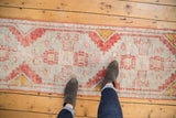 Distressed Oushak runner with brick rust, saffron, and blush rose stepped patterns, even wear.