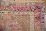 Distressed Oushak rug corner with blush, blue, ivory patterns, visible wear, and fringed end.