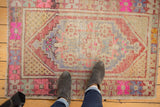 Distressed Oushak rug corner detail with geometric lozenge, blush pink, and visible knot heads.