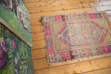 Vintage distressed Oushak rug with faded geometric pattern in vibrant pink, gold, and blue.