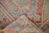 Distressed vintage Oushak rug fold showing worn pile with visible foundation, geometric pink motifs.