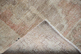 Distressed Oushak rug pile showing wear and visible hand-knotted backing, with a secured edge.