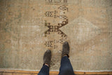 Distressed Oushak runner's worn texture, exposed foundation, and faded dark geometric motifs.