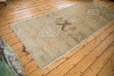 Corner of distressed vintage Oushak runner showing fringe, worn pile, and exposed foundation.