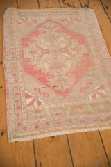 Corner of a distressed Oushak rug showing blush pinwheel motifs, ivory field, and fringe.