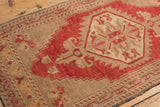 Distressed Oushak rug's diamond medallion in pale cherry red and neutral tones.