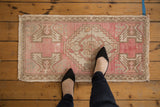 Distressed Oushak rug mat in pale pink and neutral tones, highlighting textured wear and scale.