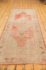 Distressed Oushak runner end, blush-beige tones, faint wear, vine border, short fringe.