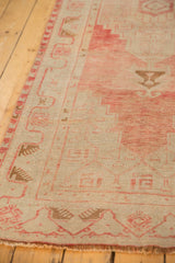 Textural close-up of distressed vintage Oushak rug, blush meandering vine border, and ivory field.