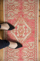Blush pink and ivory distressed Oushak rug, oversized serrated medallion, with feet in black shoes.
