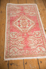 Distressed vintage Oushak rug corner, blush pink geometric motifs, fringe, and wear showing foundation.