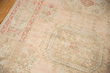 Distressed Oushak rug texture with soft blush tones and worn Kufic border motif.