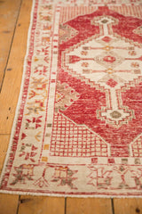 Cherry red and ivory distressed Oushak rug corner, showing geometric border and textured pile.