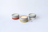 Gold-dipped concrete candle burning, flanked by red and white vessels.