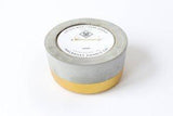 Round gold-dipped concrete scented soy candle with a white product label.