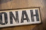 Distressed black 'ONAH' letters on the Katonah sign with dark wood frame.