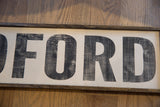 Vintage style sign detail: distressed black 'FORD' letters and dark wood frame.