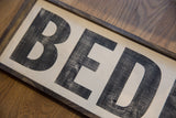 Vintage Bedford sign with distressed black 'BED' lettering on cream wood, dark frame.