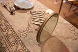 Antique shaving mirror, patinaed frame, extended white accordion arm on a patterned textile.