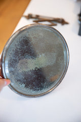 Circular surface of antique shaving mirror with dark, mottled patina and greenish hues.